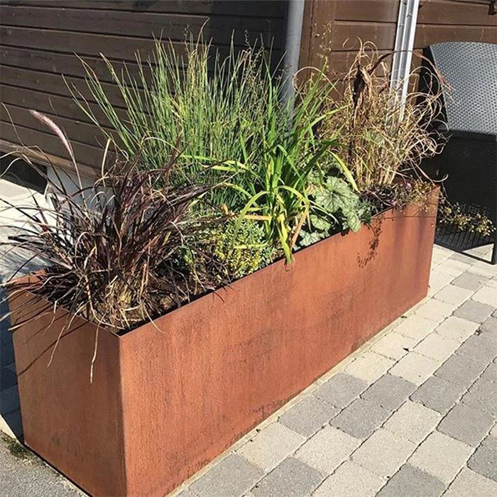 Rust-colored metal planter with green plants on a paved area