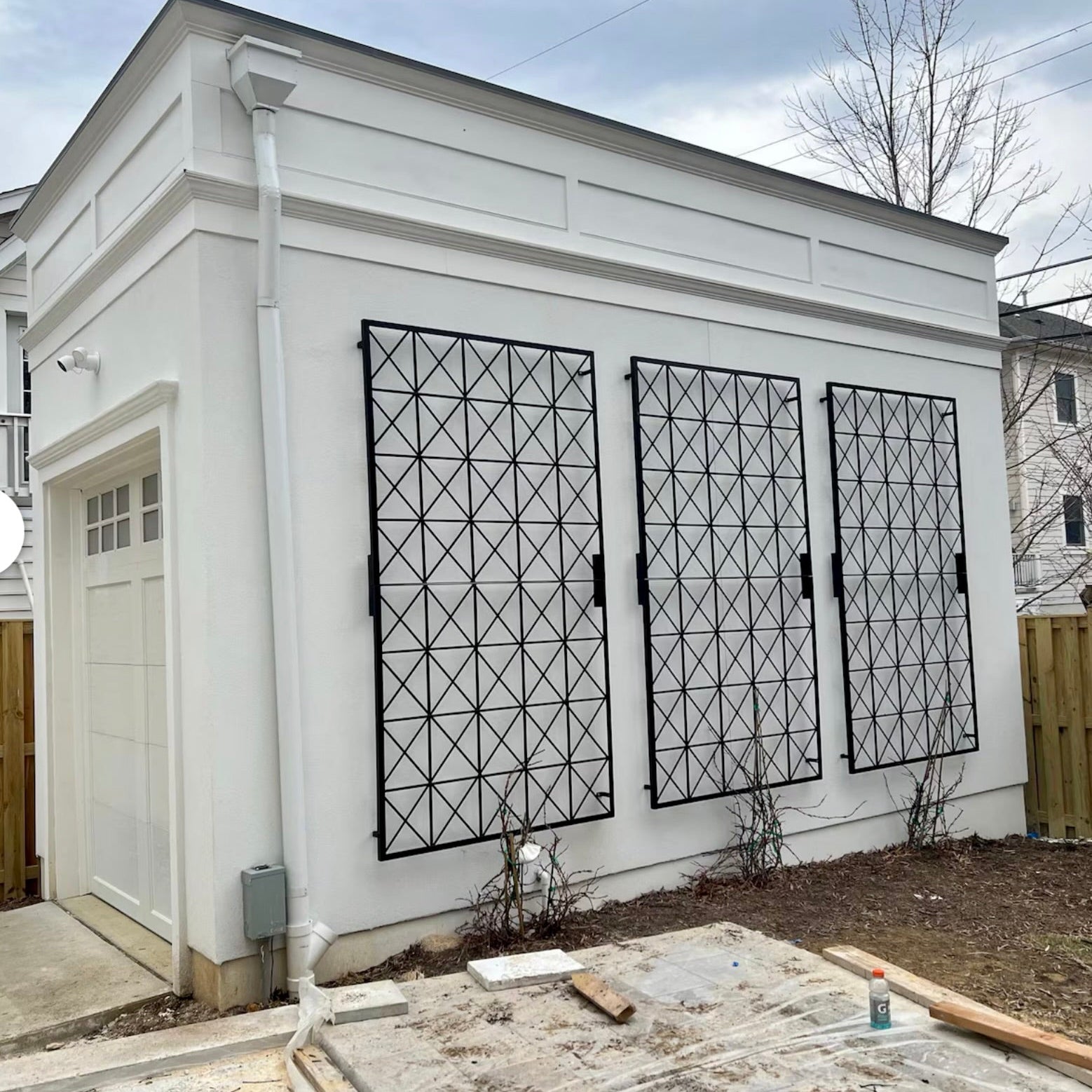 3 metal barn-style square plant trellis mounted on the side of a white building.
